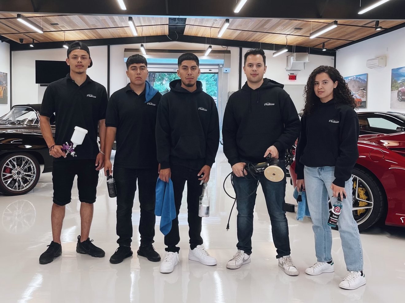 The Platinum Pit Crew, five team members in Platinum shirts and hoodies holding detailing tools in a collector car showroom